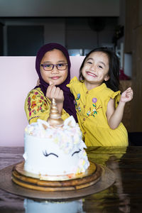 Portrait of cute girls sitting by cake at home