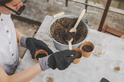 Hands in gardening gloves caucasian teenage girl put soil in a cardboard glass with a wooden spoon