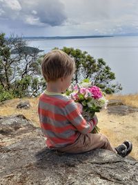 Rear view of boy sitting on shore against sky