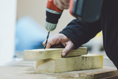 Midsection of carpenter drilling wood on table in workshop