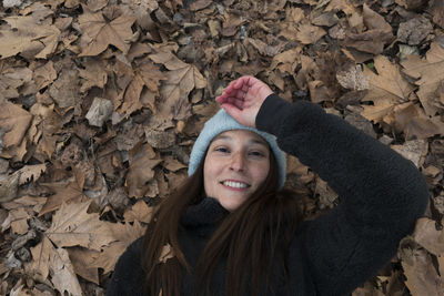 High angle portrait of smiling woman lying on autumn leaves