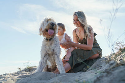 Low section of people with dog sitting against sky