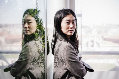 Portrait of young woman standing against window