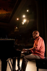 Side view of focus bald male musician playing piano during performance on obscure stage in theater