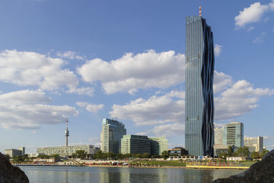 Modern buildings by river against sky in city