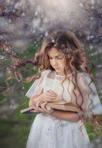 Beatiful little girl with long hair reads a book in a flowered garden 