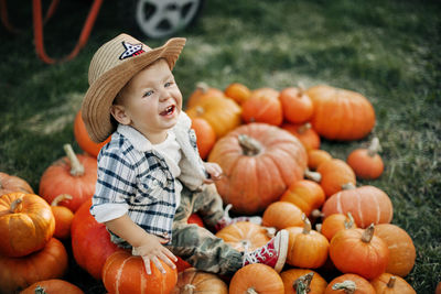 A laughing kid in a cowboy hat sits on bright orange pumpkins. holiday, halloween