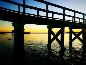 Silhouette bridge over river against sky during sunset