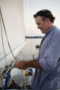 Side view of happy man tying rope while standing at yacht