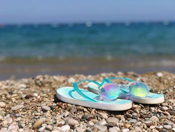 Sunglasses is on pflip flops on pebbles on beach against the sea