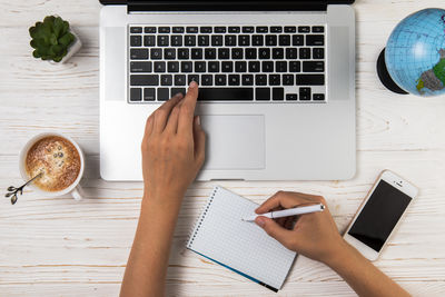 Cropped hands of woman using mobile phone on table