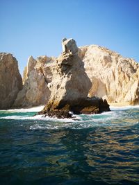 Scenic view of rocks on sea against clear sky