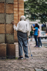 Full length rear view of senior man walking on sidewalk against people in city
