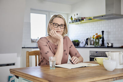 Portrait of mature woman with notebook at kitchen table