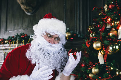 Man wearing santa claus costume holding bauble at home