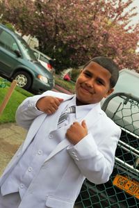 Portrait of boy standing in suit against cars