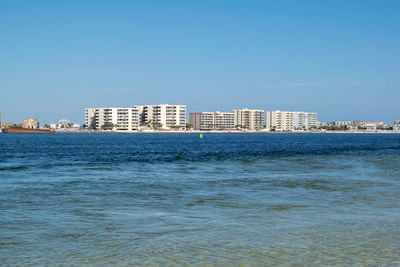 Sea by buildings against clear blue sky