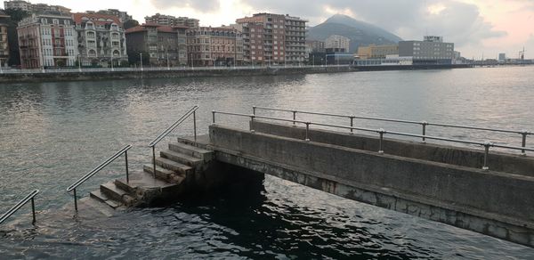 Bridge over river by buildings in city against sky