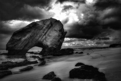 View of rocks at calm sea against clouds