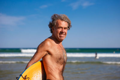 Portrait of shirtless man at beach against sky