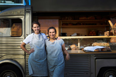 Portrait of smiling female owners standing arm around outside food truck