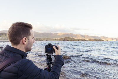 Man photographing river against sky