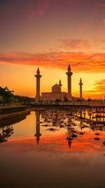 Reflection of silhouette buildings in water against orange sky