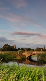 Arched bridge over a river by building against sky