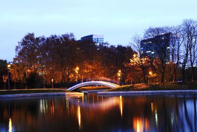 Bridge over river in city against sky at dusk