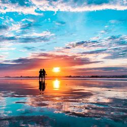 Silhouette people at beach against dramatic sky during sunset