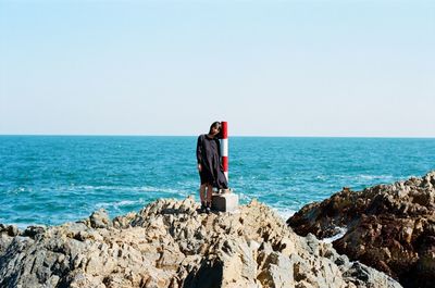 Scenic view of woman standing on rock against sea