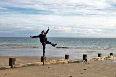 Full length of man standing on groyne at beach against sky