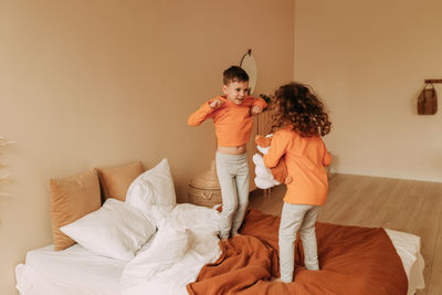 Funny happy kids brother and sister in pajamas playing having fun in a cozy bedroom at home