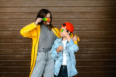 A girl in a yellow raincoat and a boy in a red cap are holding colorful ice cream in their hands