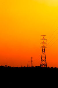 Silhouette electricity pylon against orange sky