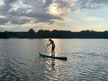 Silhouette man rowing boat in lake against sky during sunset