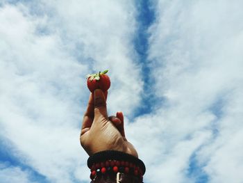 Cropped hand holding strawberry against cloudy sky