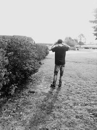 Rear view of man standing on field against clear sky