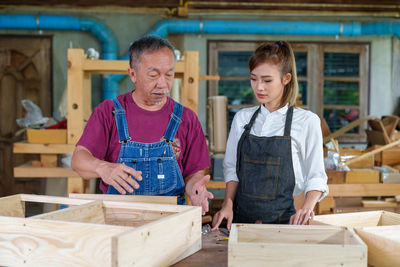 Tutor with female carpentry student in workshop studying for apprenticeship at college ,