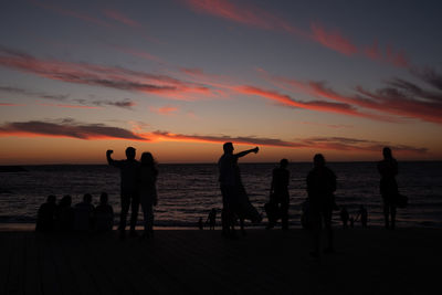 Silhouette people on beach against sky during sunset