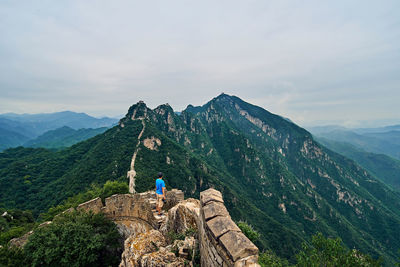 Rear view of man and woman standing on rock against sky