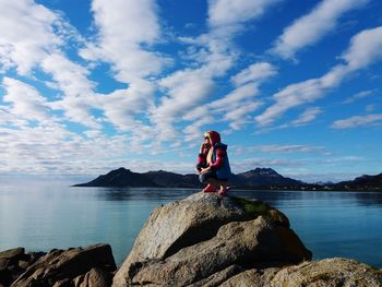 Woman crouching on rock against sea at beach