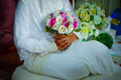 Low section of bride holding bouquet while sitting on sofa