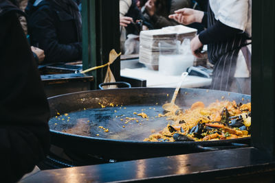 Large pan of paella at a street food market, unidentifiable people on the background.