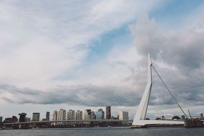 Erasmusbrug over river by modern buildings against cloudy sky