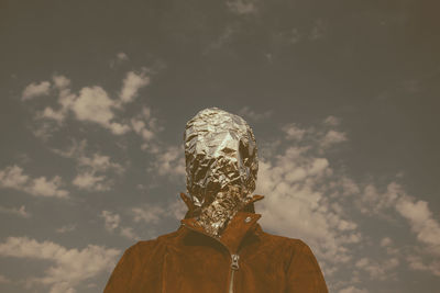 Man with face covered in foil standing against sky