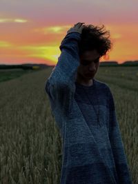 Teenage boy with hand in hair standing on land against sky during sunset