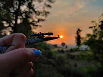 Midsection of person holding umbrella against sky during sunset