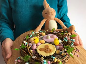 Woman holding  bamboo board with iced cupcakes and chocolate easter eggs in a decorative nest shape.