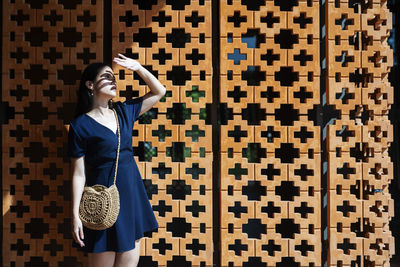 Young woman shielding eyes standing against wall